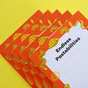 Può includere: Una pila di blocchi note arancioni e gialli con un tema di pasta. Il blocco note superiore ha il testo "Endless Pastabilities" stampato su di esso.