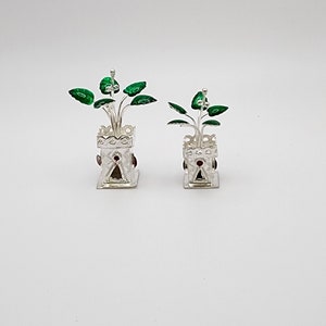 May include: Two silver potted plants with green leaves and red accents. The pots are decorated with intricate designs.