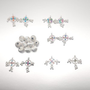 May include: Assortment of silver jewelry charms and beads. The charms feature colorful enamel designs with various symbols and patterns. The beads are round and have a textured surface.