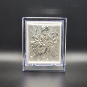 May include: A silver-toned, three-dimensional image of a Hindu goddess riding a lion. The image is framed in a clear plastic case.