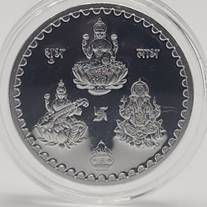 May include: Silver coin with three deities, Lakshmi, Saraswati, and Ganesha, depicted in relief. The coin features the text "Shubh Laabh" in Hindi, which translates to "Good Fortune".