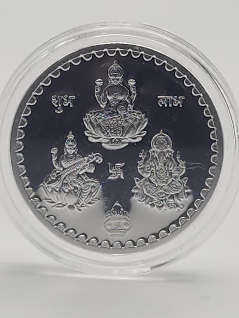 May include: Silver coin with three deities, Lakshmi, Saraswati, and Ganesha, depicted in relief. The coin features the text "Shubh Laabh" in Hindi, which translates to "Good Fortune".