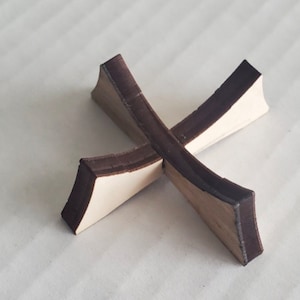 May include: A wooden cross-shaped stand with a dark brown stain. The stand is made of two pieces of wood that are joined together in the middle.