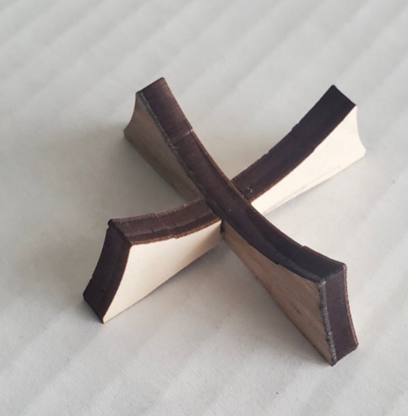 May include: A wooden cross-shaped stand with a dark brown stain. The stand is made of two pieces of wood that are joined together in the middle.