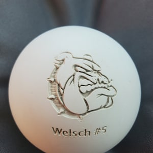 May include: White ceramic ball with an engraved image of a bulldog and the text "Welsch #5".