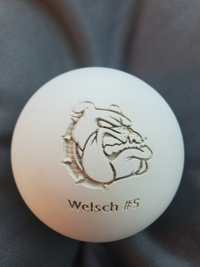 May include: White ceramic ball with an engraved image of a bulldog and the text "Welsch #5".