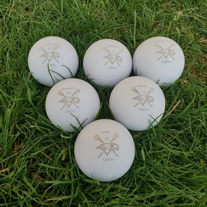 May include: Six white lacrosse balls with black and gray lacrosse stick and eagle logos. The balls are labeled with the names and numbers of players: Hansen 50, Meredith 34, Kump 30, Adams 13, and Bingham 25. All balls have the word "Eagles" printed on them.