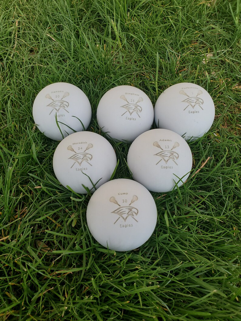 May include: Six white lacrosse balls with black and gray lacrosse stick and eagle logos. The balls are labeled with the names and numbers of players: Hansen 50, Meredith 34, Kump 30, Adams 13, and Bingham 25. All balls have the word "Eagles" printed on them.