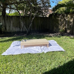 May include: A wooden platform with a white satin tablecloth on a grassy lawn.