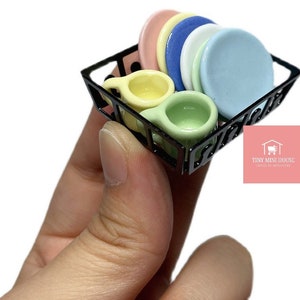 以下が含まれることがあります： 黒色のミニチュア金属製食器乾燥ラックに、パステルカラーのセラミック製のカップ4つとパステルカラーのセラミック製のプレート5つが置かれています。ラックはカップとプレートでいっぱいです。ラックは手で持たれています。