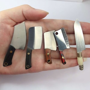 Könnte beinhalten: Fünf Miniaturmesser mit schwarzen und hölzernen Griffen. Die Messer haben silberne Klingen und sind auf einer Hand angeordnet.