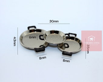 May include: Three miniature silver pans with black handles. The largest pan is 43mm in diameter, the medium pan is 30mm, and the smallest pan is 35mm. The pans are designed for a dollhouse or miniature setting.