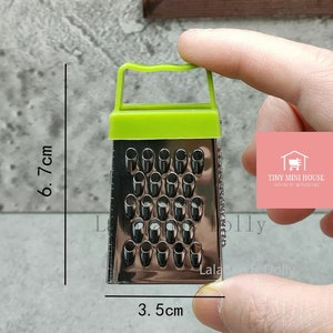 Op de afbeelding: Een miniatuur groene en zilveren rasp met een handvat. De rasp is 3,5 cm breed en 6,7 cm hoog.