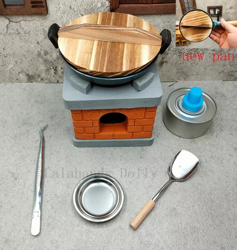 Op de afbeelding: Miniatuur keukenset met een wok, fornuis en accessoires. De wok heeft een houten deksel en staat op een grijs en oranje bakstenen fornuis. Extra items zijn een kleine metalen kom, spatel, pincet en een brandstofpatroon.