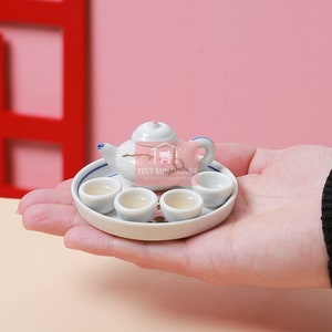 Könnte beinhalten: Ein Miniatur-Porzellan-Tee-Set mit einer Teekanne und vier Tassen auf einem weißen Tablett. Das Set ist mit einem Blumenmuster verziert und hat einen blau-weißen Rand.