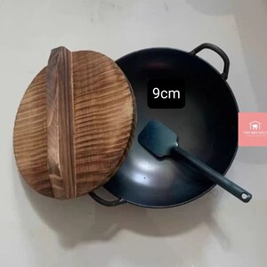 Op de afbeelding: Een 9 cm zwarte gietijzeren wok met een houten deksel en een zwarte spatel.
