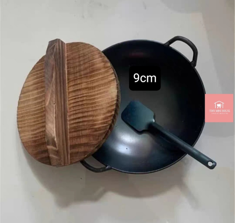 Op de afbeelding: Een 9 cm zwarte gietijzeren wok met een houten deksel en een zwarte spatel.