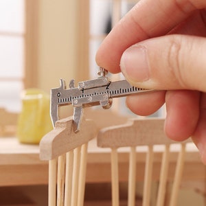 May include: A silver metal caliper measuring the width of a wooden craft project. The caliper has a measurement scale in inches.