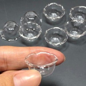 Pode incluir: Conjunto de sete tigelas de vidro transparente com bordas festoneadas. As tigelas são pequenas e perfeitas para decoração de casas de bonecas ou artesanato em miniatura.
