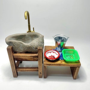 May include: A miniature stone sink with a brass faucet, a small wooden table with a green plastic basket, a red and white bowl, and a silver bucket.