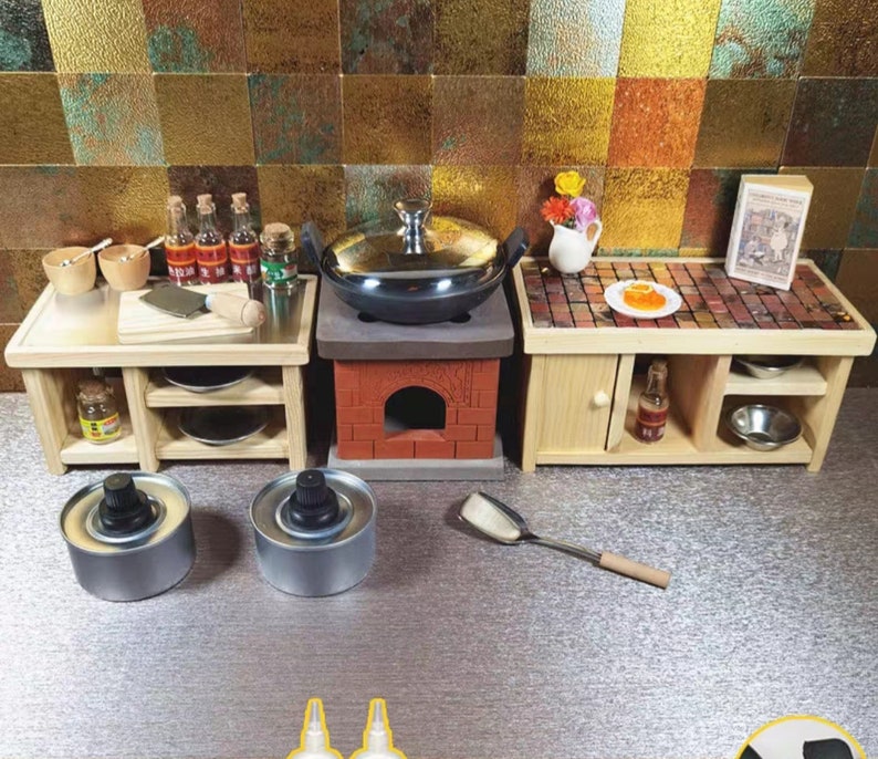 Op de afbeelding: Miniatuurkeuken met houten kasten, een bakstenen fornuis en een roestvrijstalen pot. Inclusief kleine kommen, flesjes, een snijplank en een spatel. Ontworpen voor een poppenhuis of miniatuurtentoonstelling.