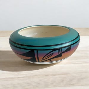 May include: A teal and white ceramic bowl with a geometric design in black and orange. The bowl has a glossy finish and is hand-painted.