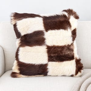 May include: A square throw pillow featuring a high-pile, textured faux fur surface with a prominent checkerboard pattern. The design consists of alternating large blocks of deep chocolate brown and creamy off-white fur, creating a bold contrast.