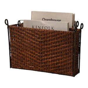 May include: A rectangular dark brown woven wicker magazine holder with a metal frame featuring looped handles at the top corners. The holder contains two light-colored books with the visible text Openhouse and KINFOLK printed on their covers.
