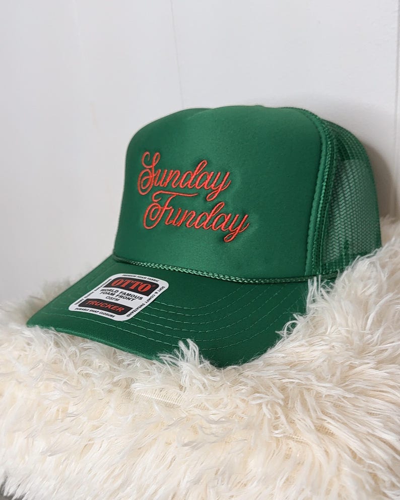 May include: A green trucker hat with the words "Sunday Funday" embroidered in red script. The hat has a mesh back and a curved brim. A white and black label is on the brim.
