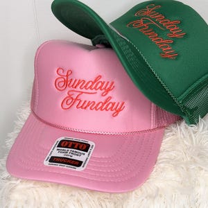 May include: Two trucker hats, one pink and one green, with the embroidered text "Sunday Funday" in a cursive font. The pink hat has a white tag that reads "OTTO WORLD FAMOUS FOAM FRONT".