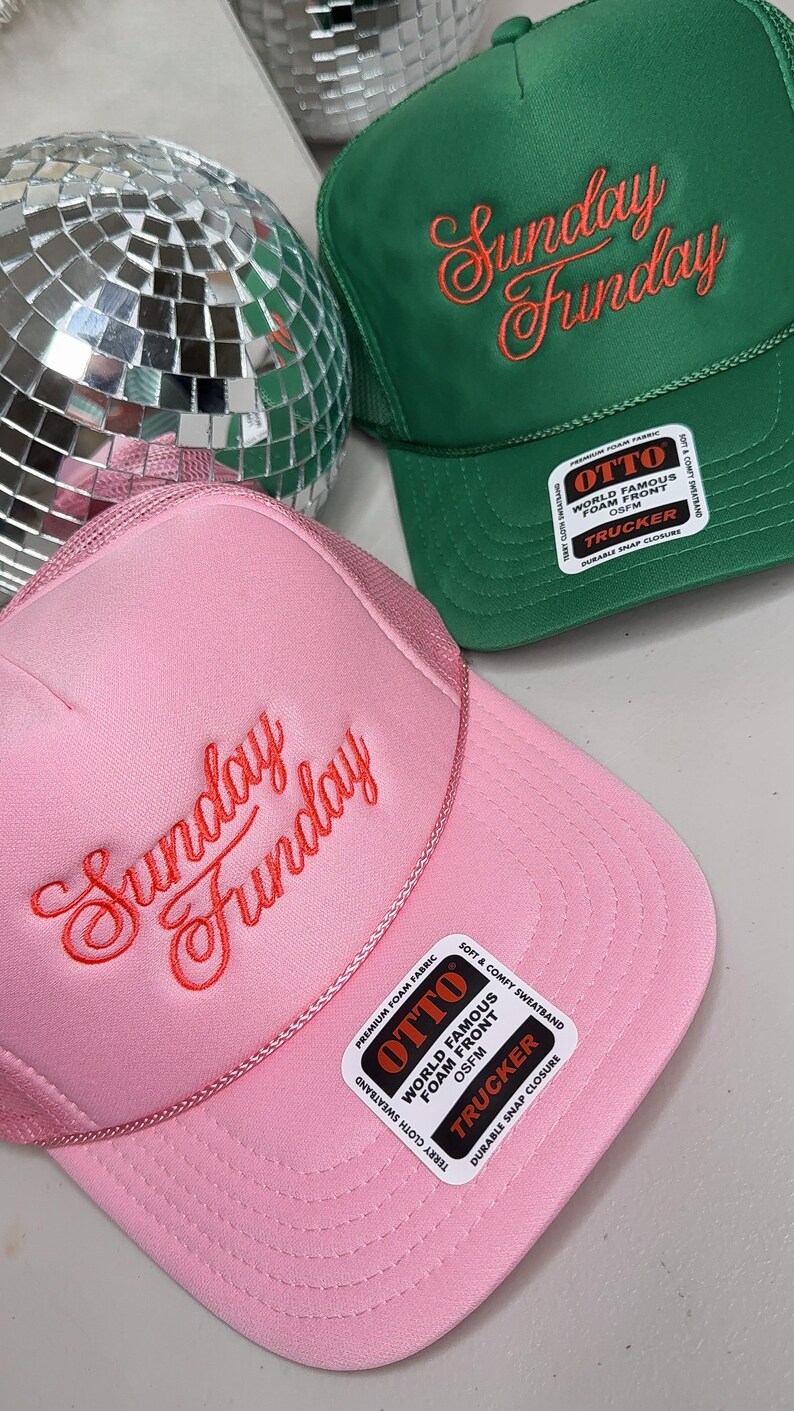 May include: Pink and green trucker hats with the text "Sunday Funday" embroidered in a cursive font. The pink hat has a matching pink mesh back, while the green hat has a green mesh back. Both hats have a "World Famous Foam Front" label.