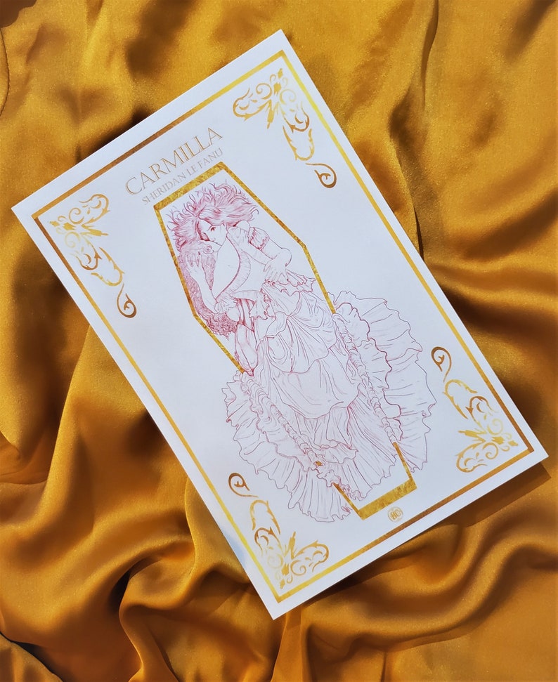 May include: A white card with gold foil accents featuring a line drawing of a woman in a coffin. The text "Carmilla Sheridan Le Fanu" is printed on the card.