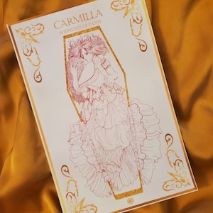 May include: A white print with a gold border featuring a line drawing of a woman in a flowing gown inside a coffin. The text "Carmilla Sheridan Le Fanu" is printed above the image.