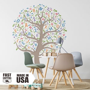 May include: A brown tree with green leaves and colorful letters spelling out the alphabet. The tree is on a white wall with a table and chairs in front of it.