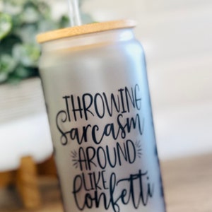 May include: A frosted glass can with a bamboo lid and a clear straw. The can has black text that reads "Throwing sarcasm around like confetti".