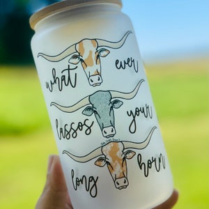 May include: White frosted glass tumbler with a bamboo lid. The tumbler features a design of three longhorn cattle with the text "what ever lassos your long horn".