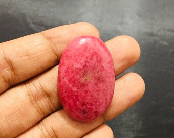 May include: An oval-shaped cabochon gemstone featuring a vibrant magenta and deep pink mottled surface with subtle dark inclusions. The stone has a smooth, polished finish and a rounded dome profile, displaying natural color variations throughout.