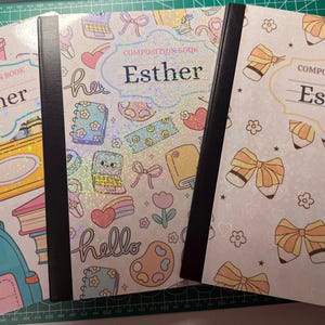 Può includere: Tre quaderni con rilegatura nera e copertina bianca che riportano il nome Esther su un'etichetta centrale. Il quaderno a sinistra presenta uno zaino, quello centrale varie icone e quello a destra fiocchi e matite di colore giallo.