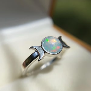 Puede incluir: Un anillo de plata con un diseño de triple luna y una piedra de ópalo blanco.