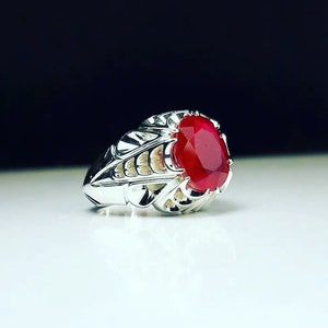 May include: A silver ring with an ornate design and a large, oval-shaped ruby gemstone.