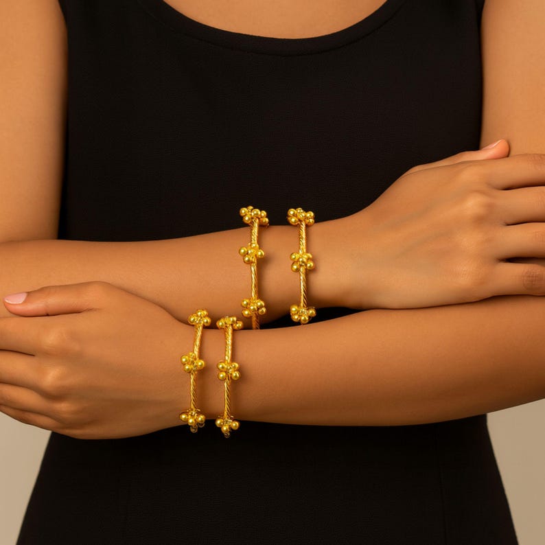 Puede incluir: Cuatro pulseras doradas se muestran en las mu&ntilde;ecas. Cada pulsera presenta un dise&ntilde;o de cuerda trenzada con tres grupos de peque&ntilde;as cuentas redondas. Las joyas se destacan sobre un fondo oscuro.