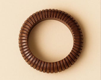 May include: A dark brown wooden bangle bracelet with a ribbed design. The bracelet is circular and has a series of vertical grooves carved around its exterior. The wood grain is visible, adding texture to the accessory.