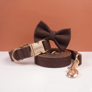 May include: A dark brown herringbone patterned pet collar with a gold-toned metal buckle engraved with the text SWING, a matching bow tie attachment, and a coiled lead featuring a gold-toned metal swivel snap hook for secure attachment.