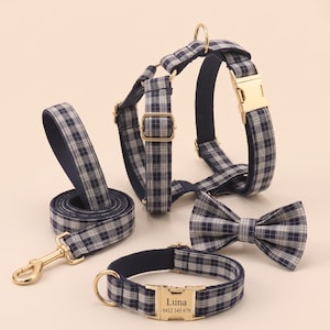 May include: A pet harness, lead, collar, and bow tie set in a navy blue and white plaid pattern. The collar features a gold-toned metal buckle engraved with the name Luna and a phone number. All items include gold-toned metal hardware and rings.