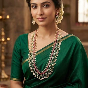 May include: A long gold necklace featuring alternating oval-shaped pink and green gemstones surrounded by small white pearls. Matching drop earrings with similar pink and green stones and pearl accents are worn with a dark green sari with gold trim.
