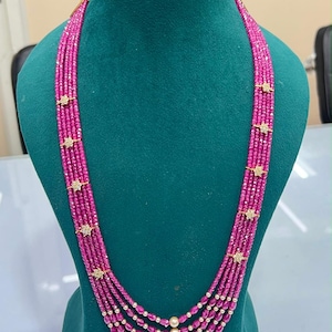 May include: A multi-strand necklace featuring five rows of faceted hot pink beads. The strands are accented with small, gold-toned star-shaped spacers and a single white pearl at the centre of each row where the strands converge at the bottom.