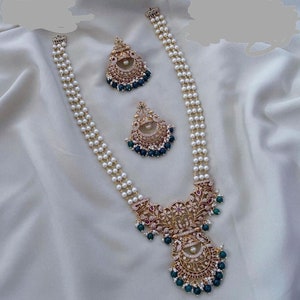 May include: A three-strand pearl necklace with a gold pendant featuring intricate floral designs and green gemstones. The pendant has a circular design with a smaller circle in the center. The necklace is accompanied by a pair of matching earrings.