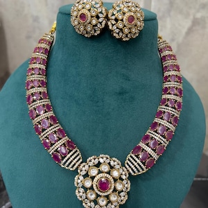 Può includere: Una collana d'oro con un grande ciondolo rotondo incastonato con pietre rosa e bianche. Il ciondolo è circondato da un cerchio di pietre rosa più piccole. La collana è abbinata a orecchini.