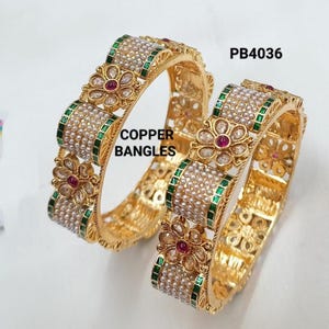 May include: Two gold-colored copper bangles with floral and pearl accents. The bangles have a repeating pattern of flowers with red centers, green borders, and pearl-like beads. The text "COPPER BANGLES" is visible.