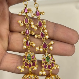 May include: A pair of long gold-tone dangle earrings featuring a vertical chain of teardrop-shaped pink stones, small white pearls, and a central green stone accent. The base of each earring consists of a bell-shaped jhumka adorned with pink stones.